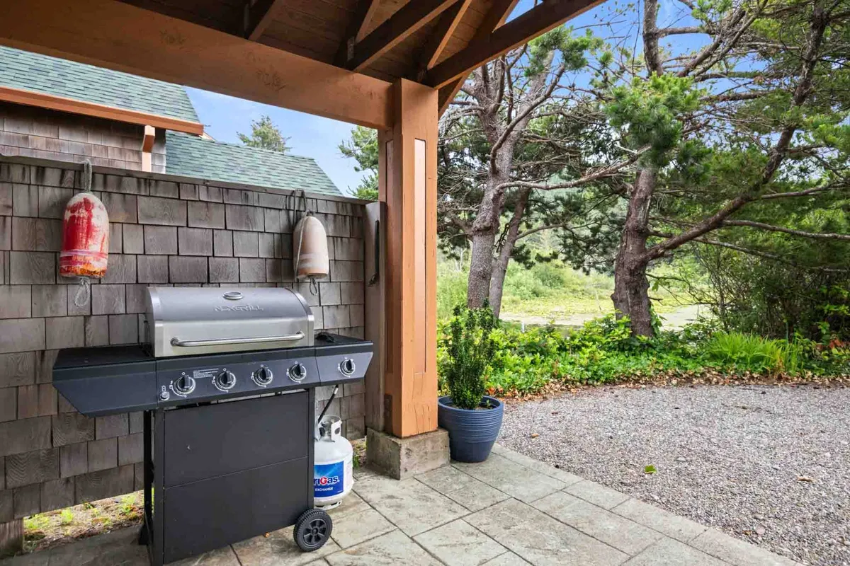 The image features an inviting outdoor grilling area with a barbecue, decorative buoys, potted plants, and lush greenery in the background. The scene emphasizes social gatherings, al fresco dining, and the enjoyment of fresh air and local flavors.