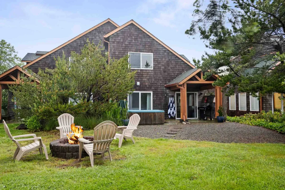 An inviting fire pit encircled by adirondack chairs sits amidst lush greenery, with the house’s exterior visible. The setup evokes a sense of gathering, warmth, and connection to the outdoors, perfect for storytelling and stargazing.