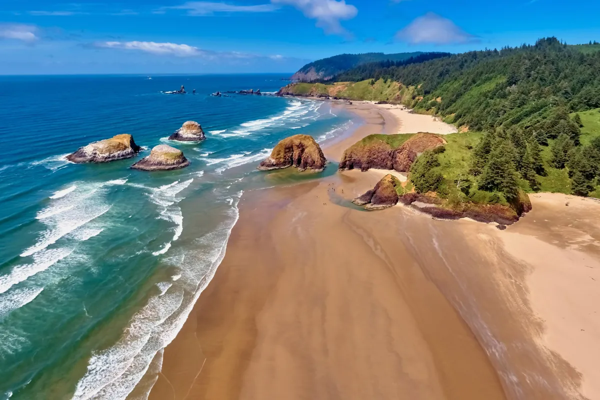 This image features a wide sandy beach bordered by dramatic rock formations and green cliffs, with ocean waves rolling in. The serene setting captures the natural beauty and peaceful atmosphere of Twin Rocks Beach, inviting viewers to imagine relaxing, exploring tide pools, or beachcombing along the shore.