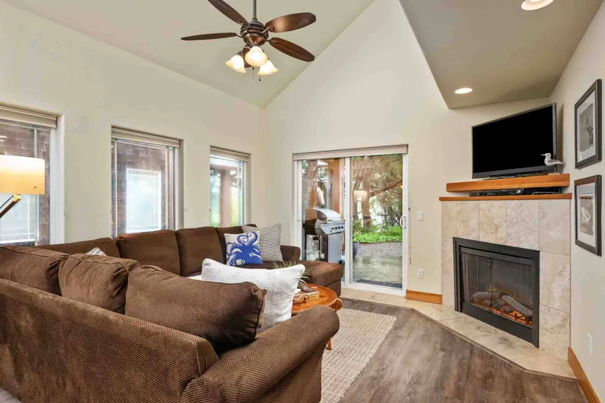 A spacious living area with a large sectional sofa, a cozy fireplace, and sliding glass doors leading to what appears to be a yard or outdoor space. The open layout and outdoor access reinforce the connection between indoor comfort and outdoor play.
