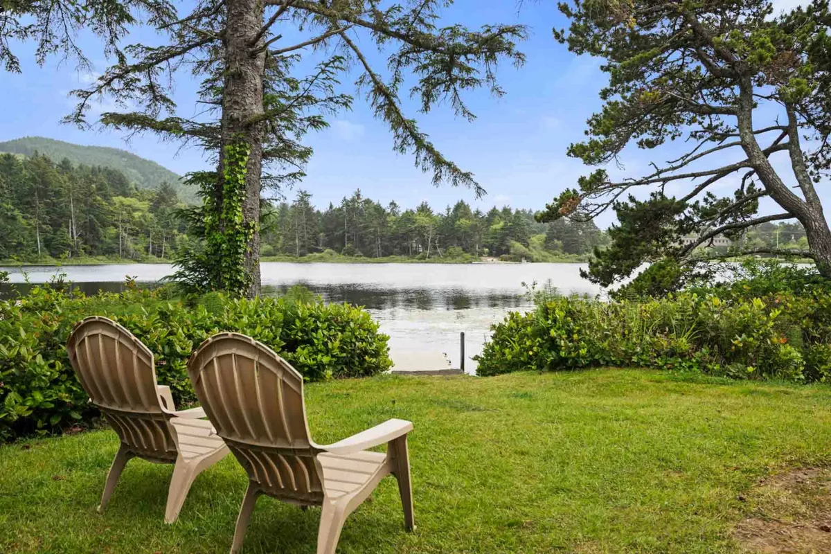 Two comfortable chairs positioned on lush green grass, facing out over the calm expanse of the lake. The natural surroundings include dense greenery and a gently rippling water surface—inviting guests to relax, read, or simply gaze at the tranquil scenery.