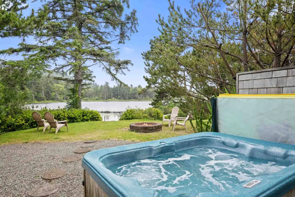 The hero image showcases the home's peaceful lakeside setting, featuring a bubbling hot tub and a cozy fire pit surrounded by comfortable lawn chairs, all overlooking the tranquil waters of Spring Lake. The scene evokes a sense of relaxation and connection with nature, with sunset colors reflecting off the water and inviting outdoor spaces perfect for unwinding or gathering with loved ones.