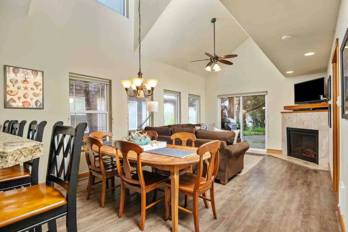 A warmly lit dining area and living space with a fireplace, dining table, sofa, and windows that bring natural brightness into the room. The setting is ideal for family meals, game nights, and relaxed conversation by the fire, embodying the sense of shared experiences and cozy comfort highlighted in the section text.