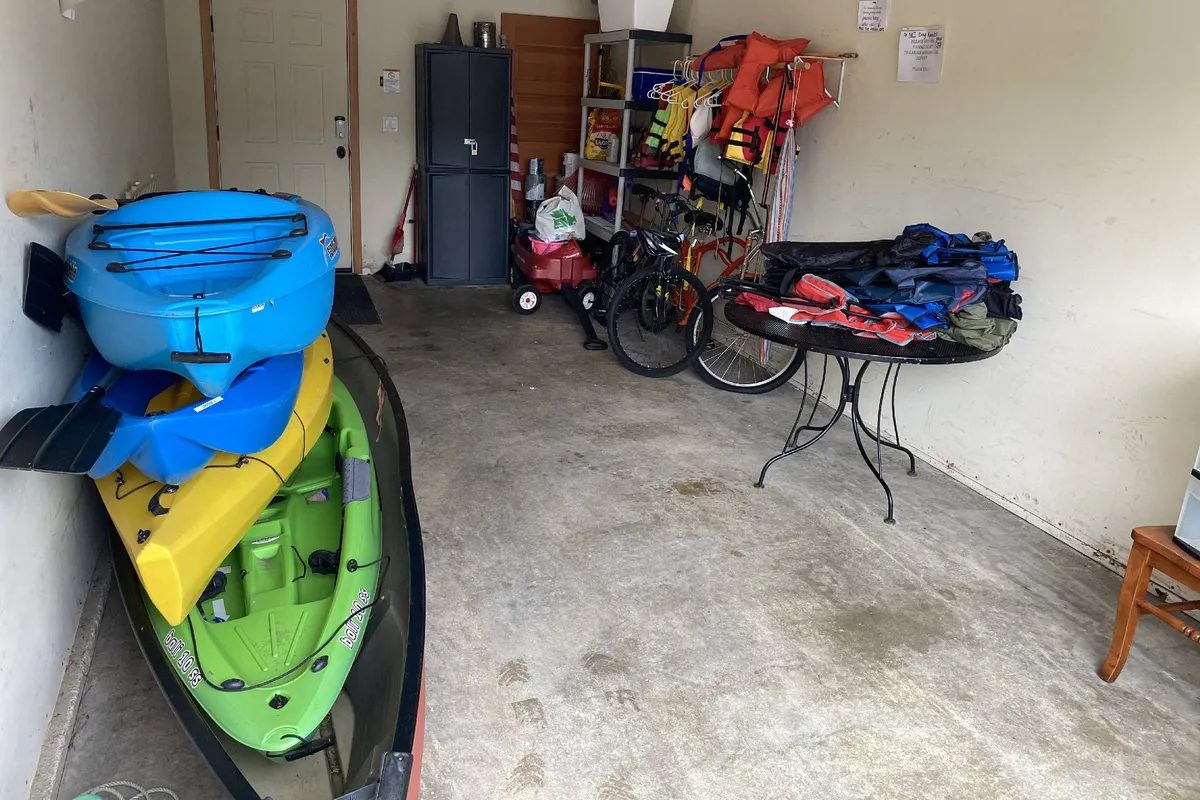 Inside the garage, several colorful kayaks are neatly stored alongside a bicycle and a variety of life vests. The space is organized and suggests readiness for outdoor adventure, with gear easily accessible for all ages and sizes.