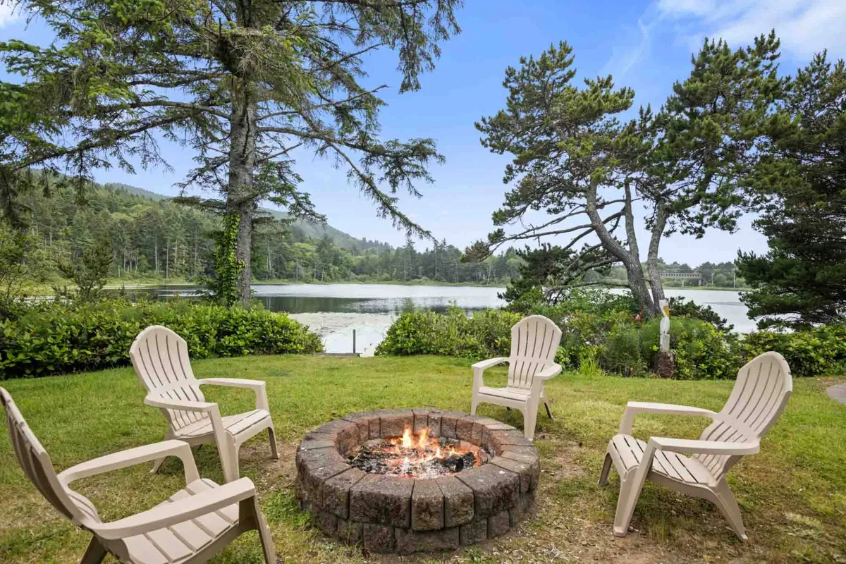 An inviting outdoor setup with a fire pit surrounded by lawn chairs, offering a cozy spot to relax while enjoying a sweeping view of the lake and surrounding trees. The atmosphere is peaceful, perfect for unwinding after a day on the water.