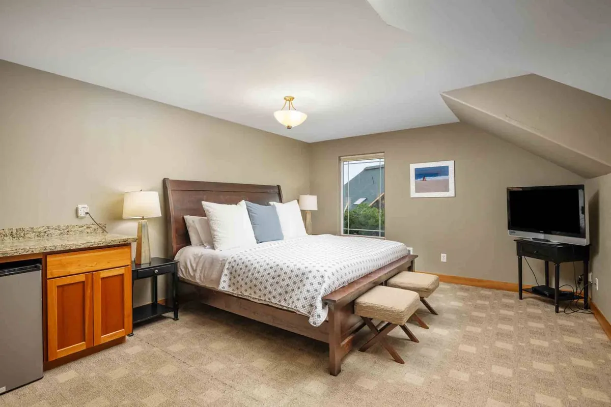 This image showcases a serene bedroom featuring white and gray bedding, a granite countertop, a window with a pleasant view, and a television. The space feels private and inviting—ideal for relaxing, reading, or enjoying a quiet moment.